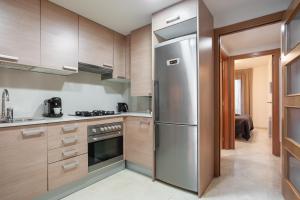 cocina con armarios de madera y nevera de acero inoxidable en ApartsNouBcn Fira Barcelona en Hospitalet de Llobregat