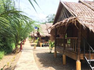 a building with a straw roof and a walkway at Khaosok Bamboo Huts Resort in Khao Sok National Park