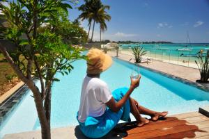 a man sitting on a bench next to a swimming pool at OBiches Luxury Beachfront Apartment Trou-aux-Biches in Trou aux Biches