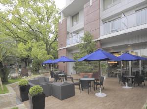 a patio with tables and chairs with blue umbrellas at K's Street Hotel Miyazaki in Miyazaki