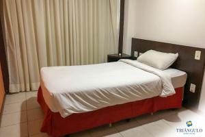 uma cama num quarto de hotel com um cobertor branco e almofada em Triângulo Apart Hotel em Vitória