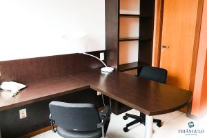 um escritório com uma secretária de madeira e 2 cadeiras em Triângulo Apart Hotel em Vitória