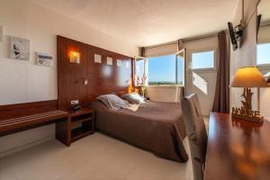 a bedroom with a bed and a desk and a window at Hotel Les Dunes in Marseillan