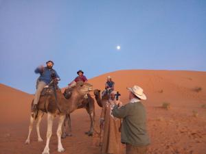 a group of people riding on camels in the desert at Riad camels house in Merzouga