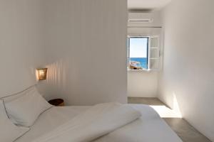 a white bedroom with a bed and a window at Perigiali Rooms & Apartments Folegandros in Agali