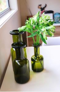 three green vases with flowers in them on a table at WoodyHanger Lodge in Whitianga