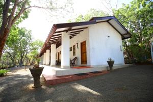 a small white house with a porch and trees at Amadi Rest in Kataragama