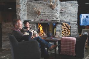 two men sitting in chairs in front of a fireplace at Santa's Hotel Aurora & Igloos in Luosto