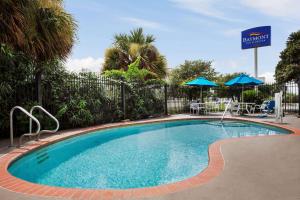 a swimming pool in a resort with tables and umbrellas at Baymont by Wyndham Clute Lake Jackson in Clute