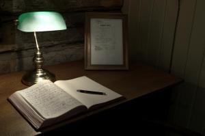 einen Schreibtisch mit einem Buch, einem Stift und einer Lampe in der Unterkunft Seljord Hotel - Unike Hoteller in Seljord