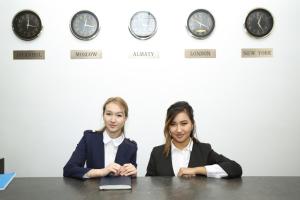 zwei Frauen an einem Tisch vor Uhren in der Unterkunft Altai Business Hotel in Almaty