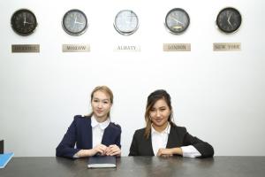 two women sitting at a table in front of clocks at Altai Business Hotel in Almaty