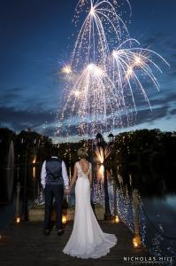 a bride and groom standing under a fireworks display at Inn On The Lake in Gravesend