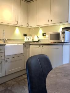 una cocina con armarios blancos y una silla azul en Coniston Cottage Lake View en Coniston