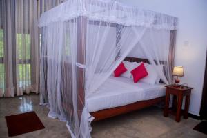 a bedroom with a white canopy bed with red pillows at Villa Greenary in Unawatuna