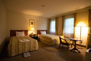 a hotel room with two beds and a table and a chair at Kyu Karuizawa Hotel Otowa No Mori in Karuizawa