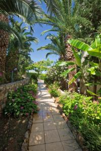 a walkway in a garden with flowers and palm trees at Rethymno Mare & Water Park in Skaleta