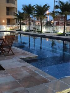 a chair sitting next to a swimming pool with palm trees at Loft Condado Aldeia dos Reis 216 in Mangaratiba