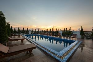 a swimming pool with benches and a sunset in the background at Azalea Parkview Hotel in Vientiane