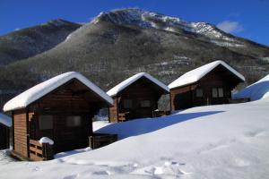 un groupe de huttes recouvertes de neige devant une montagne dans l'établissement Camping Laciana Natura, à Villablino