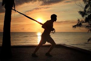 a man swinging a pole on the beach at sunset at Tulia Zanzibar Unique Beach Resort in Pongwe