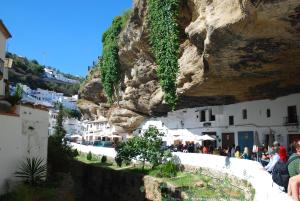 a group of people sitting on a wall next to a mountain at Casa cueva de la sombra in Setenil