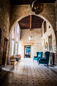 a living room with two blue chairs and a stone wall at Dar Camelia in Soûr