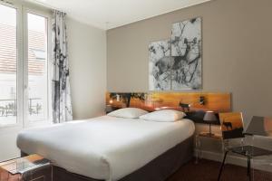 Un dormitorio con una gran cama blanca y una ventana. en Hotel Le Cardinal Rueil Centre, en Rueil-Malmaison