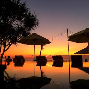 a pool with chairs and umbrellas in front of a sunset at Twilight Ceningan in Nusa Lembongan