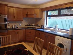 La cuisine est équipée de placards en bois, d'un évier et d'un lave-vaisselle. dans l'établissement Torrent Cottage, à Coalisland