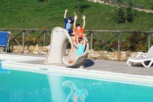 Drei Kinder springen von einer Rutsche in ein Schwimmbad in der Unterkunft The Assisi at Pian Di Cascina (Umbria with Kids) in Carbonesca