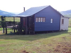 a blue house with a porch in a field at The Tin Shack in Underberg
