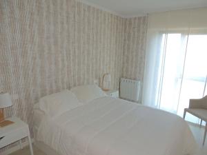 1 dormitorio con cama blanca, silla y ventana en Apartamento romántico con el mar a tus pies, en Ribeira