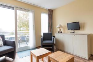 sala de estar con TV y sillas y balcón en Appartement De Vrijbuiter, Resort Amelander Kaap en Hollum