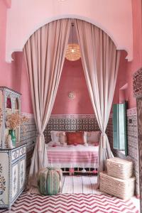 Riad BE Marrakech في مراكش: غرفة نوم بجدران وردية وسرير والستائر