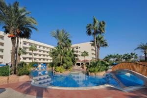 a large swimming pool with palm trees in front of a hotel at Nissiana Hotel & Bungalows in Ayia Napa
