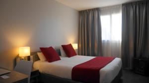a hotel room with a bed with red pillows and a window at Hotel L'Hotan in Portet-sur-Garonne