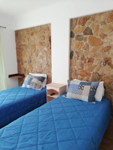 two blue beds in a room with a stone wall at Sol Mar in Odeceixe