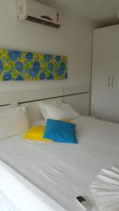 Una cama blanca con una almohada azul y amarilla. en Condomínio Mont Hebron - Apto 3A, en Porto Seguro