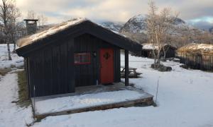 Eine schwarze Hütte mit roter Tür im Schnee in der Unterkunft Northern gate Besseggen - Cottage no 17 in Besseggen Fjellpark Maurvangen in Maurvangen
