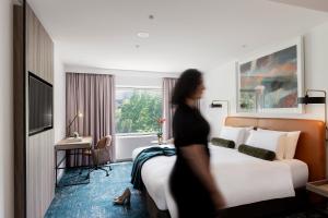 a woman walking past a hotel room with a bed at Novotel Sydney Darling Square in Sydney