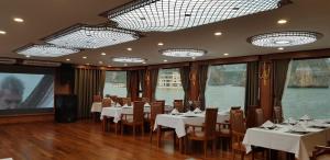 un restaurante con mesas y sillas blancas y ventanas en Calypso Cruises, en Ha Long