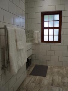 La salle de bains est pourvue de murs en carrelage blanc, d'une fenêtre et de serviettes. dans l'établissement RAFTERS COTTAGE, à Plumstead
