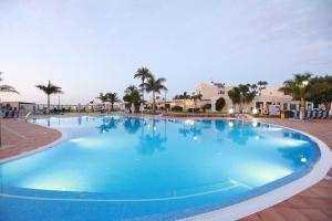 une grande piscine bleue avec des palmiers et des maisons dans l'établissement Grupotel Playa Feliz, à San Agustín