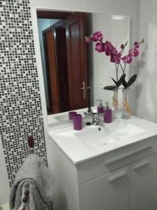 un baño con lavabo con flores púrpuras en un jarrón en VuT EL GRECO, en Salamanca