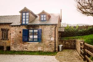 una antigua casa de ladrillo con ventanas azules y una valla en Hay Barn en New Mills