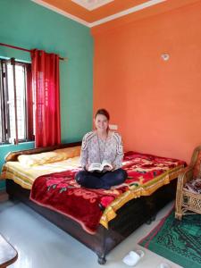 a woman sitting on a bed reading a book at Anjali Home Stay in Rishīkesh