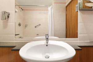 
a white sink sitting under a mirror in a bathroom at Savera Hotel South Ruislip in Hillingdon
