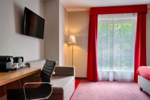 Habitación de hotel con escritorio y ventana con cortinas rojas. en Focus Hotel Katowice Chorzów, en Chorzów