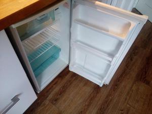 an empty refrigerator with its door open on a wooden floor at Studio Les Drus / Studio du Brévent in Chamonix-Mont-Blanc